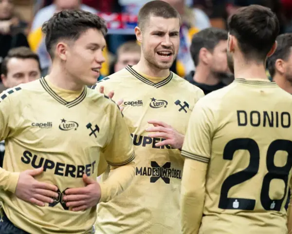 Piłkarze ręczni Górnika Zabrze w złotych strojach rozmawiają na boisku.