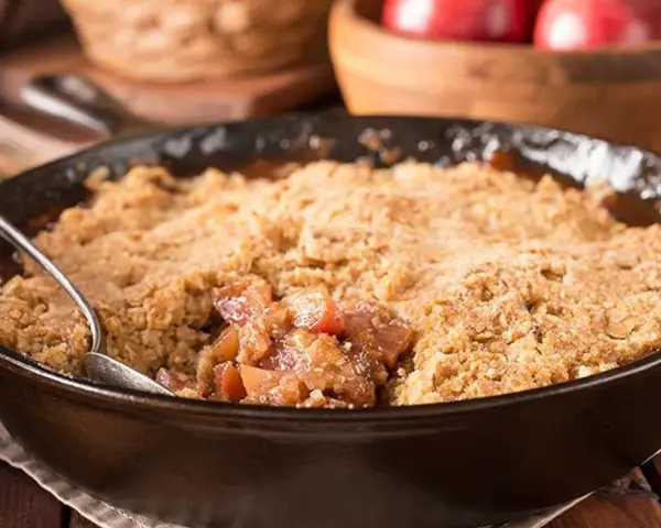 Un délice de pâte à crumble croustillante sur un lit de fruits fondants, servi dans une poêle en fonte.