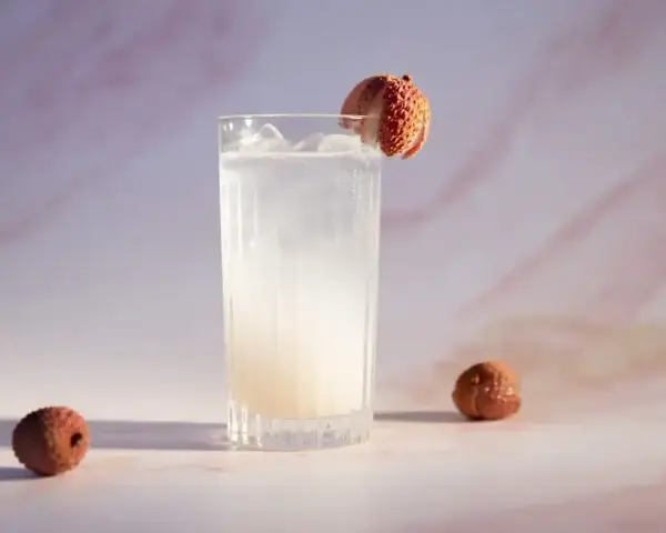 Orzeźwiający drink z liczi, ozdobiony owocem, z dwoma całymi liczi obok. Idealny na letnie popołudnie.