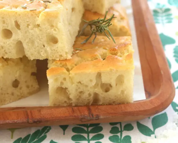 Focaccia alta e soffice, tagliata a cubetti, guarnita con rosmarino e sale grosso, servita su un tagliere di legno.