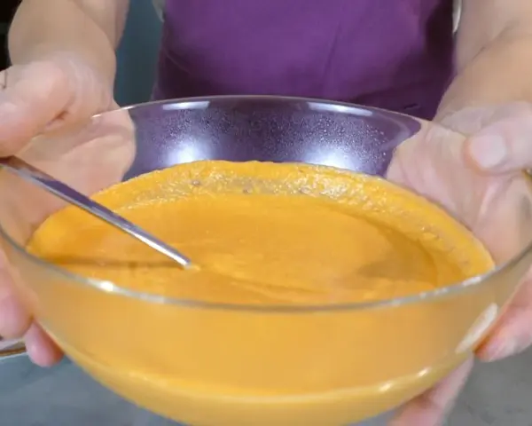 Mani che sorreggono una ciotola di vetro con una cremosa maionese di pomodoro, pronta per essere gustata.