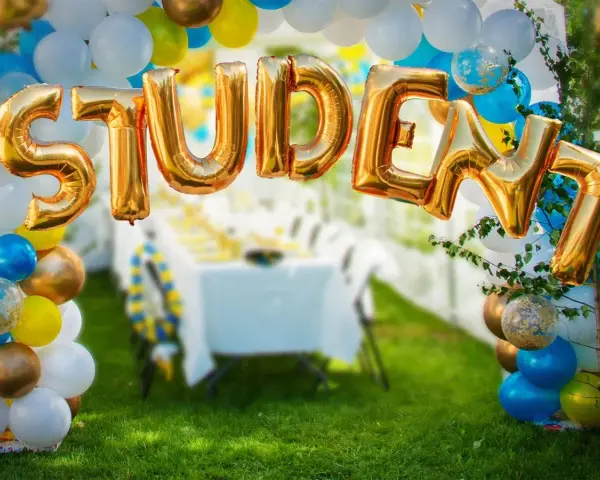 Gyllene folie ballonger bildar ordet "STUDENT" framför en festdukning utomhus.