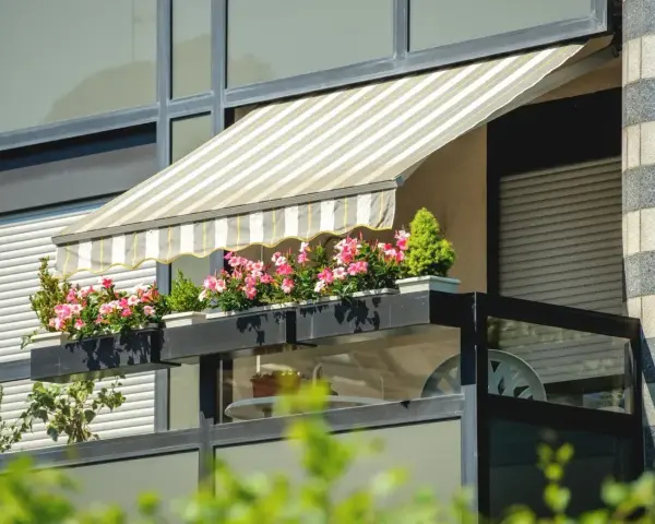 Zadaszenie balkonu z markizą i kwitnącymi kwiatami to świetny sposób, jak osłonić balkon przed słońcem i deszczem.
