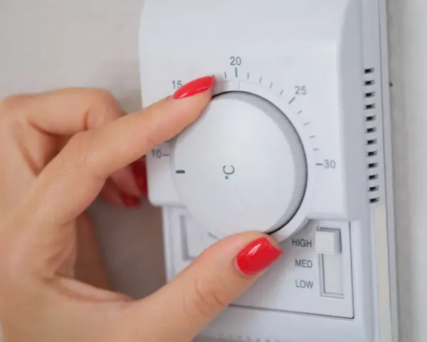 Dłoń z czerwonym lakierem reguluje termostat, ustawiając temperaturę dla elektro zaworów do CO.
