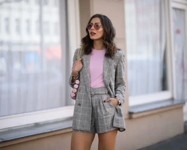 Elegancka stylizacja: co ubrac do spódnico spodenek? Szary garnitur w kratę, różowy top i modna torebka.