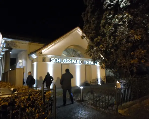 Abendliche Beleuchtung am **Schlosspark Theater**. Drei Personen nähern sich dem Eingang.