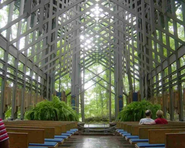 Wnętrze kaplicy w lesie, gdzie architektura organiczna łączy się z naturą. Drewniane ławki, paprocie i światło przenikające przez kratownicę tworzą spokojną atmosferę.
