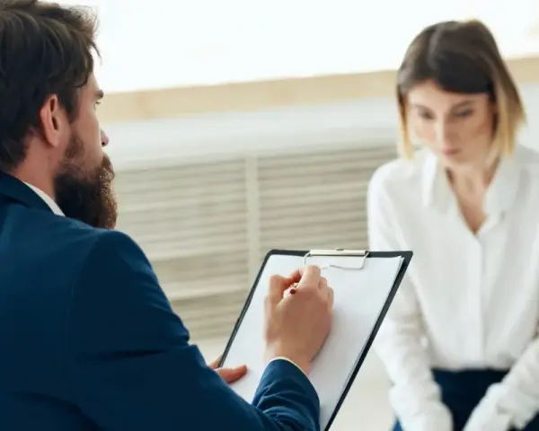 Mężczyzna z brodą w garniturze notuje coś na kartce, siedząc naprzeciwko kobiety.