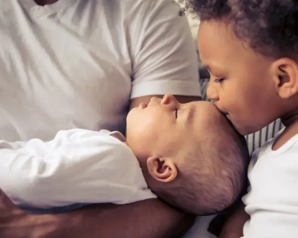 Ein älteres Kind küsst liebevoll die Stirn eines Babys. Die Frage "zweites Kind ja oder nein" scheint hier beantwortet.