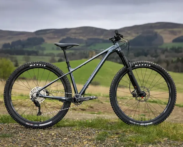 A dark grey hard tail bike with knobby tires sits on a grassy hill, ready for adventure.