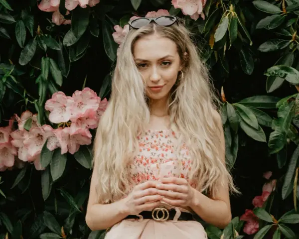 Blondynka w kwiecistej sukience, z okularami na głowie, otoczona różowymi kwiatami rododendronów. To kwintesencja słowiańskiej urody.