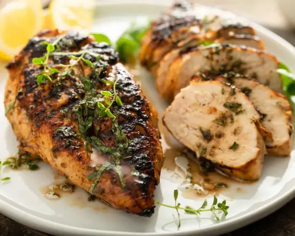 Delicioso pollo a la parrilla jugoso y tierno, con hierbas frescas y limón, servido en un plato blanco.