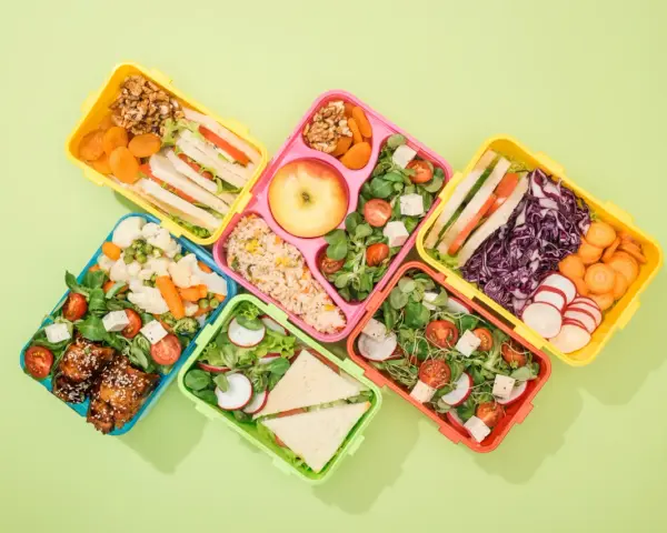 Kolorowe pojemniki na lunch z kanapkami, sałatkami, owocami i warzywami.
