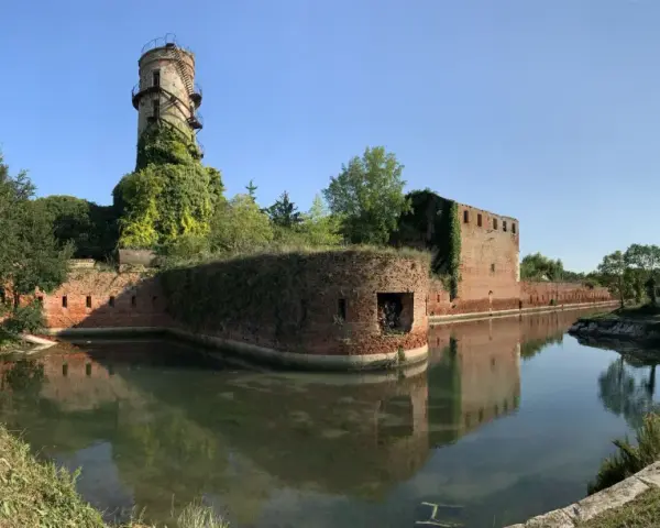 Antica torre e mura di mattoni circondate da un fossato, un angolo suggestivo di Venezia e dintorni, con vegetazione rigogliosa.