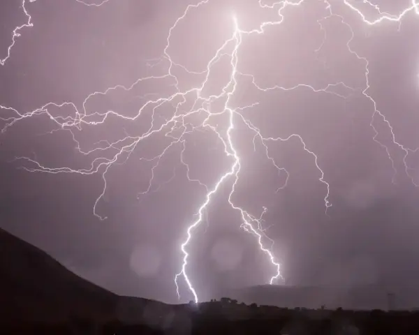 Éclairs zébrant un ciel sombre, illuminant un paysage montagneux lors d'un photo d'orage spectaculaire.