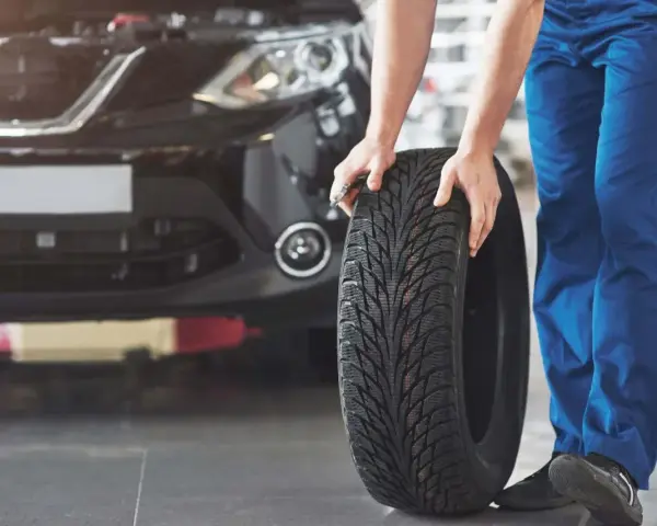Mechanik pokazuje, jak założyć opony w dobrym kierunku. Widać bieżnik i czarne auto.
