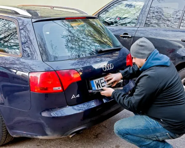 Mężczyzna montuje tablicę rejestracyjną na samochodzie Audi A4. Nowa rrs rejestracja gotowa do drogi.