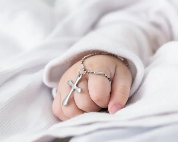 Dziecięca dłoń z krzyżykiem na srebrnym łańcuszku na białym tle.