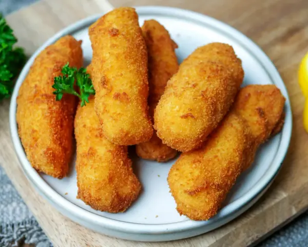 Knusprige kroketten aus kartoffelbrei, goldbraun frittiert, garniert mit Petersilie und Zitronenspalten.