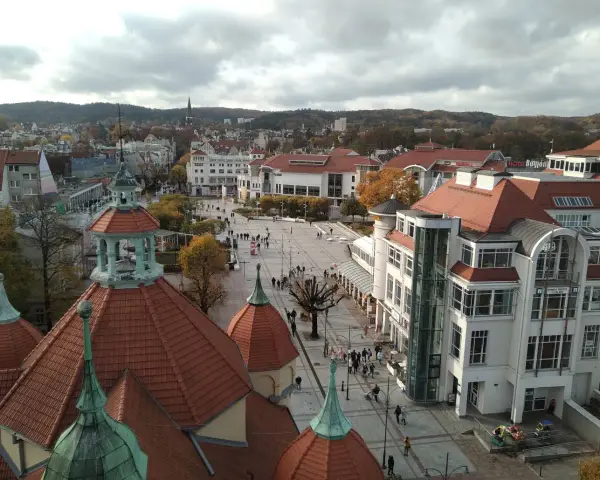 Widok na plac w Sopocie z charakterystycznymi dachami i budynkami. Wiele osób spaceruje, szukając sopotorium opinie.