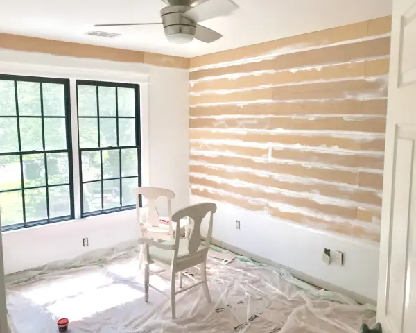 Room in progress, showing how to install shiplap on the wall. Two chairs sit on protective plastic sheeting.