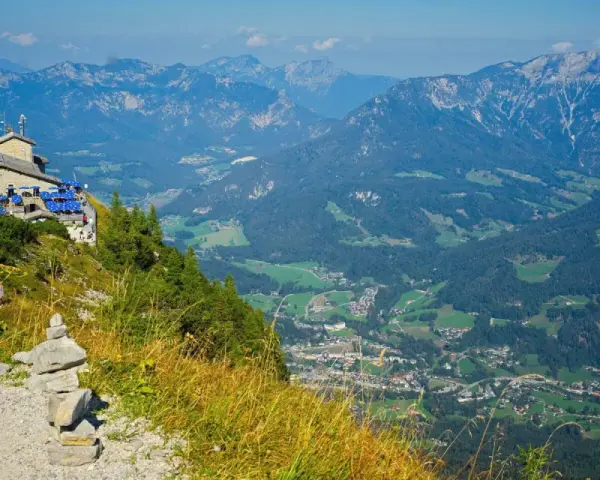 View from Hitler's Eagle's Nest, a stone building with blue umbrellas, perched high in the Bavarian Alps overlooking a valley.