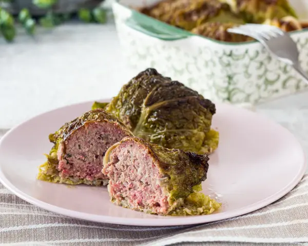 Involtini di verza con carne succulenta, uno tagliato a metà per mostrare il ripieno saporito.