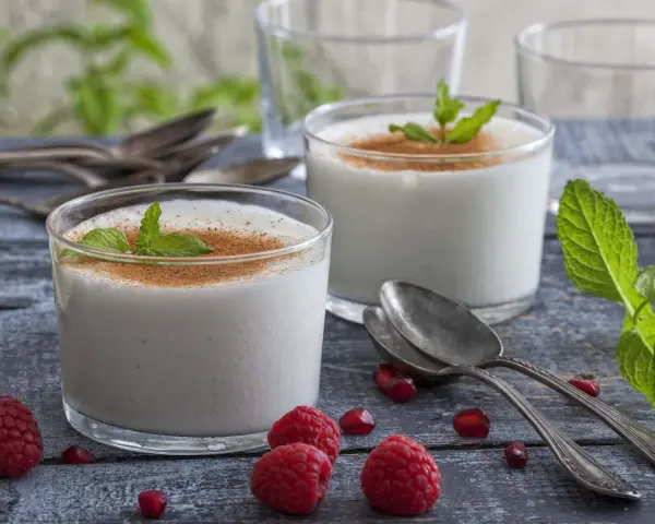 Zwei Gläser cremiger Leche Merengada, garniert mit Minze und Zimt, umgeben von Himbeeren und Granatapfelkernen.
