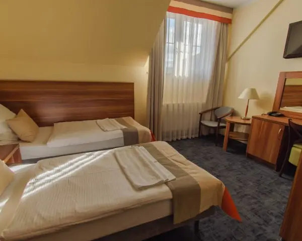 Pokój w zajazd u dziadka: dwa wygodne łóżka, stolik nocny z lampką, biurko z lustrem i krzesłem, telewizor.
