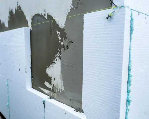 Prace nad projektem elewacji starego domu: styropian i świeży tynk na ścianie.