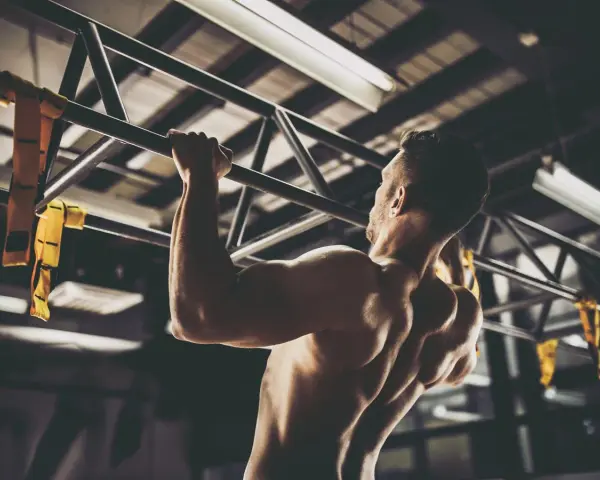 Hombre musculoso realizando pull ups en un gimnasio. Sus brazos y espalda están tensos mientras se eleva.
