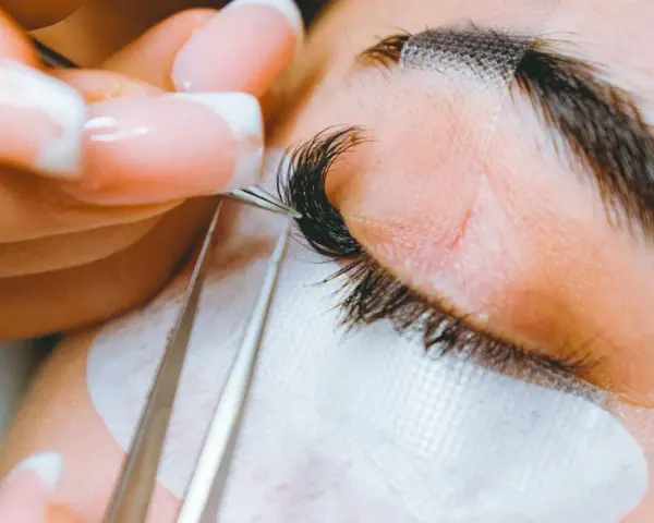 Precyzyjne przedłużanie rzęs: porównanie rzęsy 2d i 3d. Stylistka z perfekcyjnym manicurem dokłada kępki.