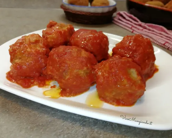 Polpette di pane al sugo, morbide e saporite, servite su un piatto bianco. Un classico della cucina italiana.