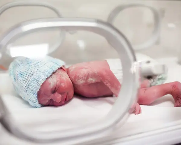 Maleńki noworodek, dziecko urodzone w 20 tygodniu ciąży, w inkubatorze, w niebieskiej czapeczce.