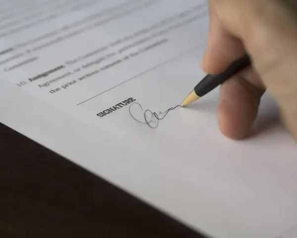 Dłoń podpisująca dokument długopisem.