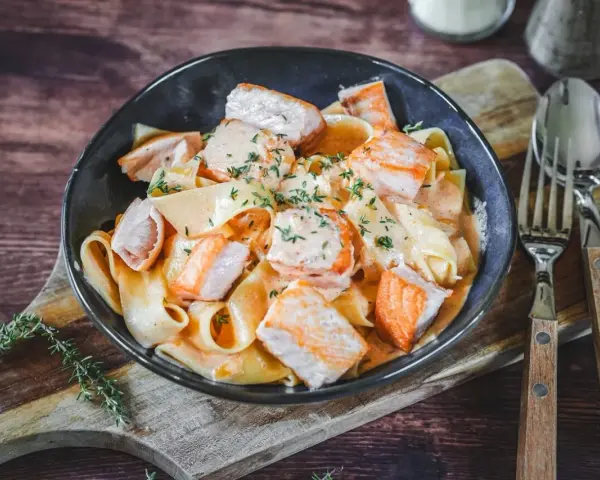 Breite Bandnudeln mit saftigen Lachs-Stücken in cremiger Lachs Sahne Sauce, garniert mit frischen Kräutern. Ein Genuss!