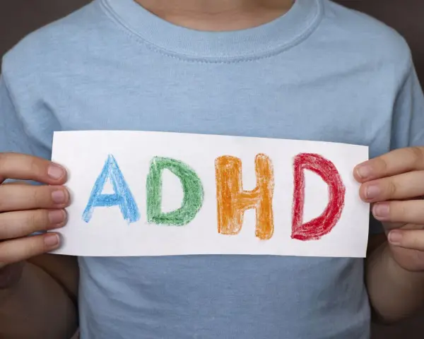 Mani di bambino tengono un foglio con la scritta "ADHD" colorata. Riconoscere i sintomi dell'ADHD è il primo passo.
