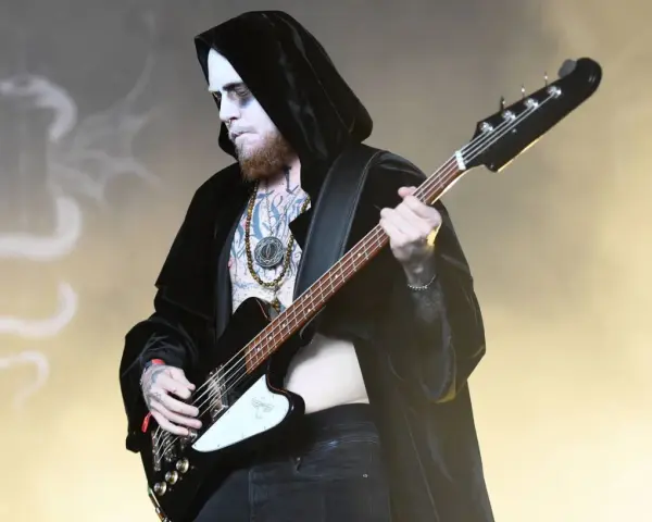 Le bassiste d'un groupe metal connu, maquillé et tatoué, joue sur scène, drapé dans une cape noire.
