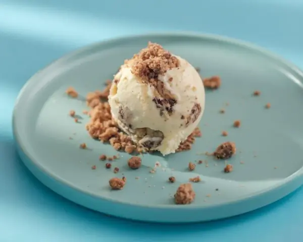 Eiscreme mit Schokoladenstückchen und Krümeln, serviert auf einem blauen Teller. Glukosesirup sorgt für die cremige Konsistenz.