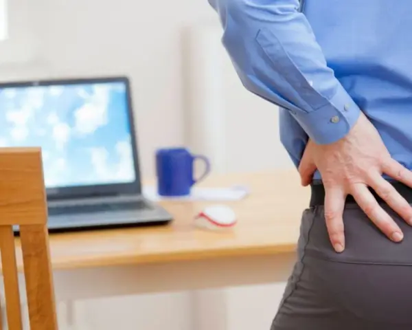 Mann mit Rückenschmerzen am Schreibtisch. Eine krankenhaustagegeldversicherung sinnvoll, um bei Krankheit abgesichert zu sein.