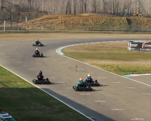 Gara di go-kart su pista con piloti in azione. Sullo sfondo, un cartellone pubblicitario con la scritta "Ottobiano Motorsport".