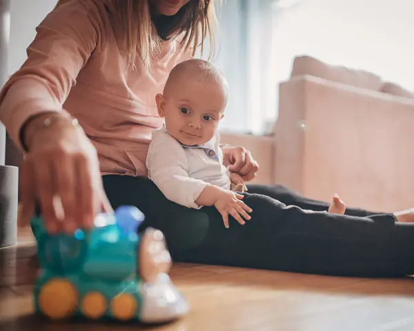 Mama bawi się z 9-miesięcznym dzieckiem, podając mu kolorową zabawkę-pociąg.