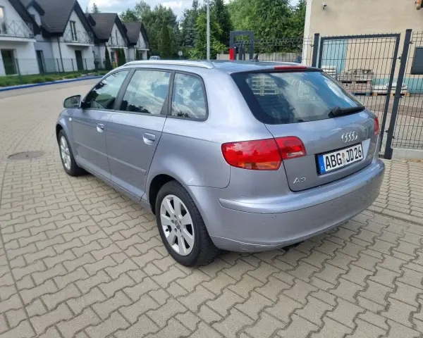 Srebrny Audi A3 kombi zaparkowany na kostce brukowej, w tle domy i drzewa.