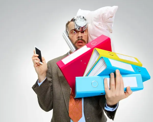 Uomo stressato con pile di cartelle, telefono e cuscino in testa. Lo stress aumenta il cortisolo, che fa ingrassare.