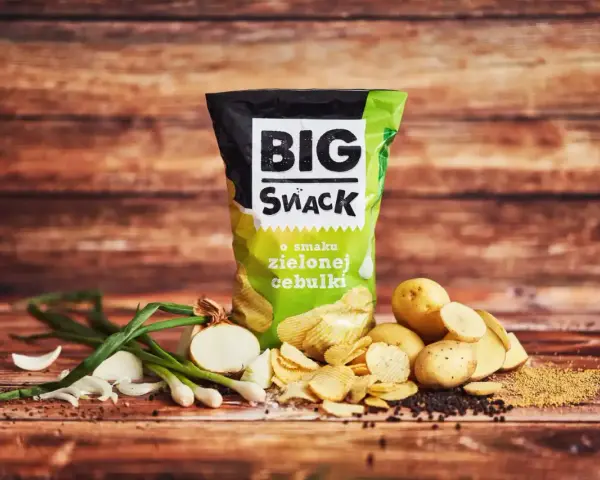 Reklamowa fotografia chipsów Big Snack o smaku zielonej cebulki, z ziemniakami i cebulką.