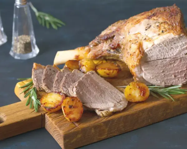 Un gigot de 7 heures, tendre et juteux, servi avec des pommes de terre rôties et du romarin sur une planche en bois.