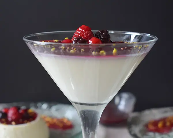 Deliciosa panna cotta receta, cremosa y adornada con frutos rojos y pistachos. Un postre elegante.