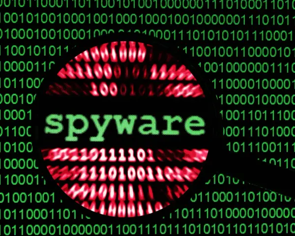 Lupa sobre código binario verde y rojo, con la palabra "spyware" en verde en el centro.