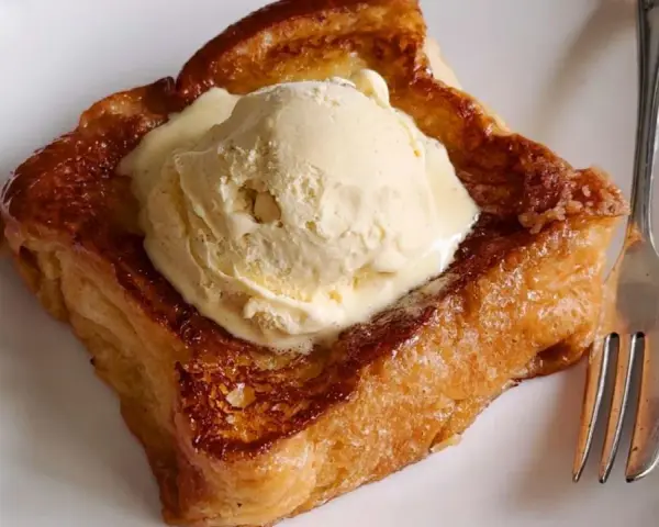 Torrijas con pan brioche, doradas y crujientes, coronadas con una generosa bola de helado de vainilla. Un postre irresistible.