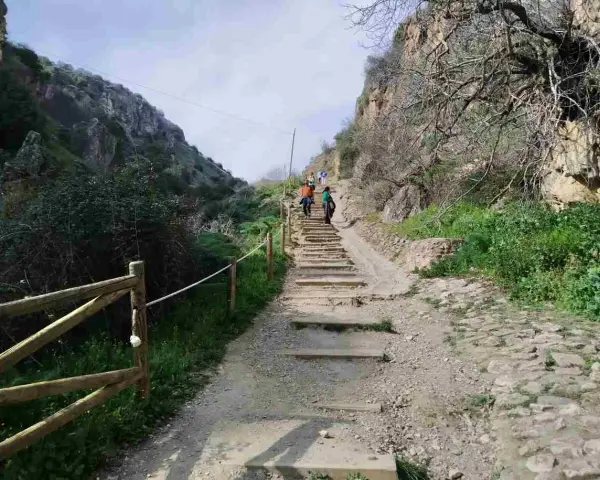 Senderos de montaña con escalones de piedra y madera. Personas caminan por las rutas Patones de Arriba, rodeadas de vegetación y acantilados.